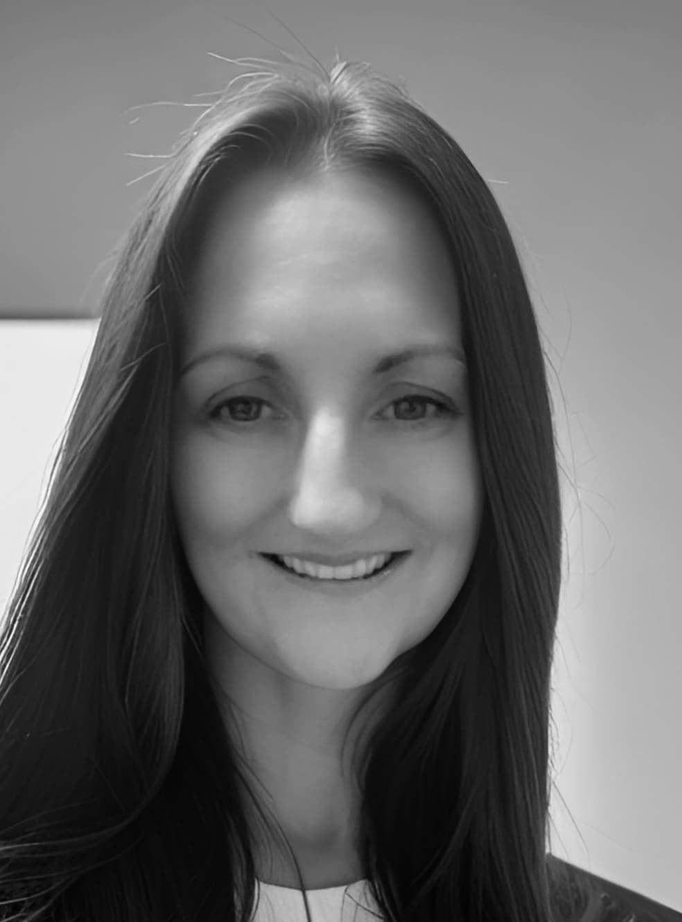 Close-up black and white portrait of a woman with long hair smiling warmly.